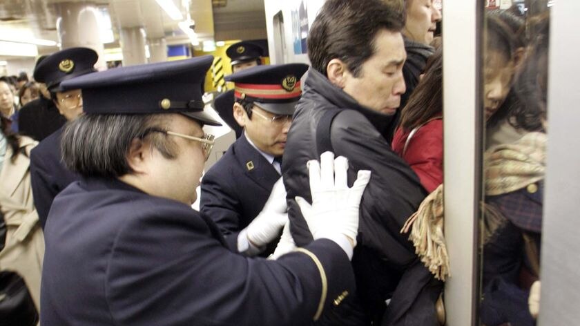 Station workers push passengers into a crowded subway train