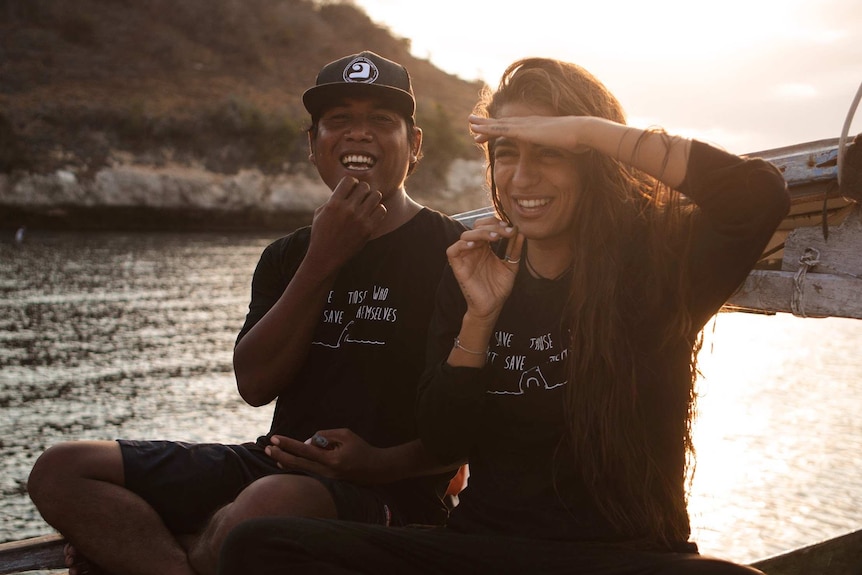 A man and a woman sit on a boat, sheltering their eyes from the sun