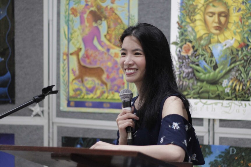 A woman smiling and speaking with posters in the background.