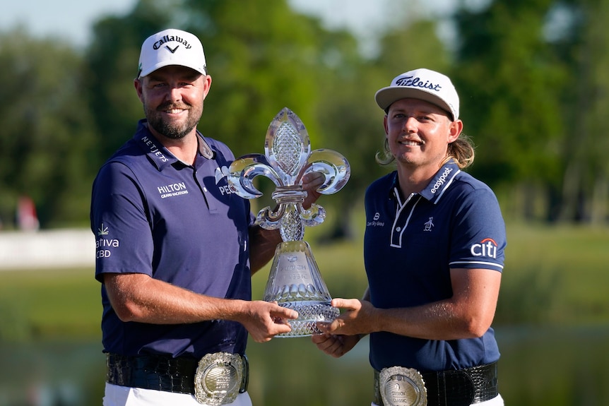 Two golfers smiling while holding the winning trophy for a photo 