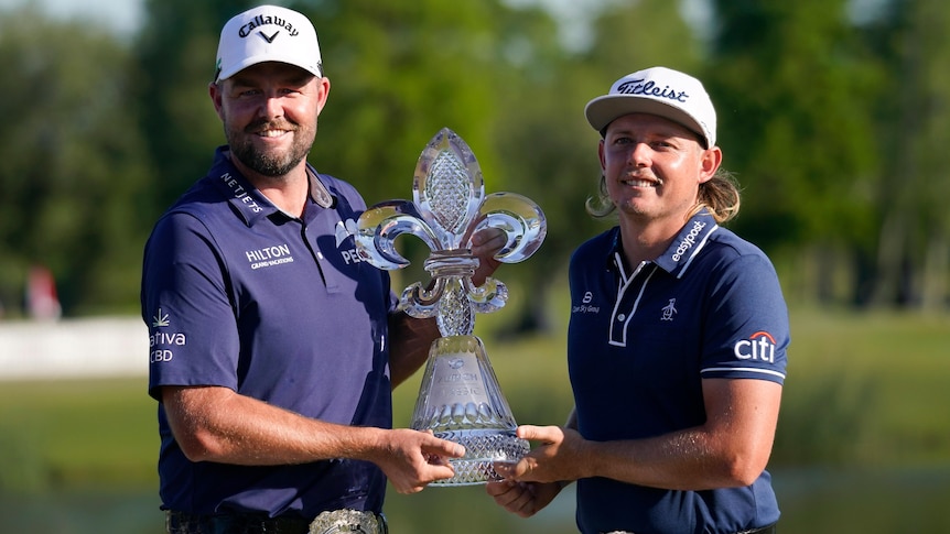 Two golfers smiling while holding the winning trophy for a photo 