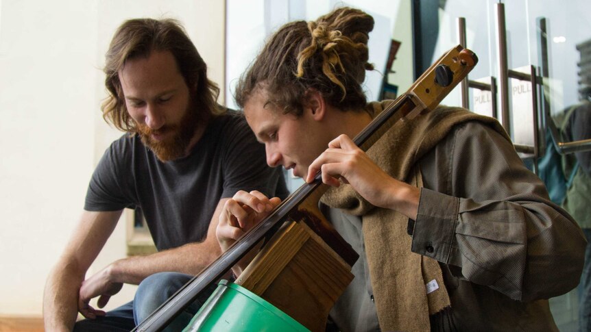 Daniel Biederman and Nils Hobiger sit around a 'cello' made from a green oil drum.