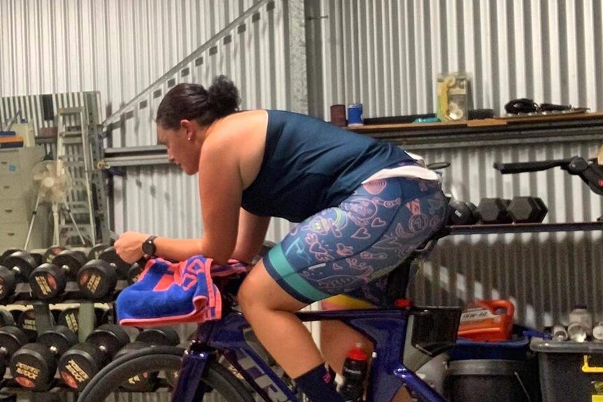 Woman riding on stationary bike in garage with, profile view.