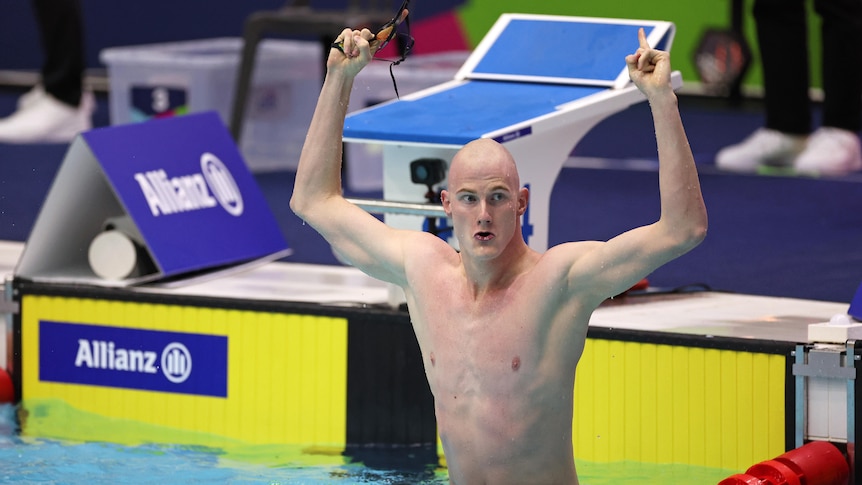 An Australian para-swimmer stands in the pool with his arms raised and fists clenched in celebration.