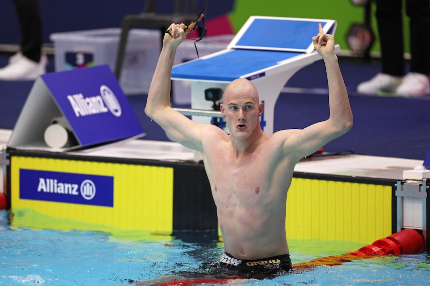 An Australian para-swimmer stands in the pool with his arms raised and fists clenched in celebration.
