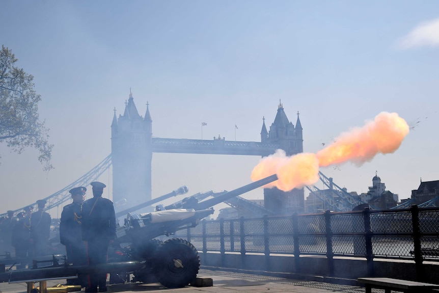 Large artillery guns fire with London's Tower Bridge in the background.