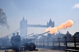 Large artillery guns fire with London's Tower Bridge in the background.