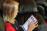 A blond child whose face is turned away from the camera sits on a couch and uses an iPad.