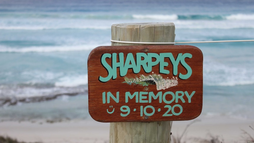 A hand painted timber sign saying Sharpeys in memory 9.10.20 on a beach