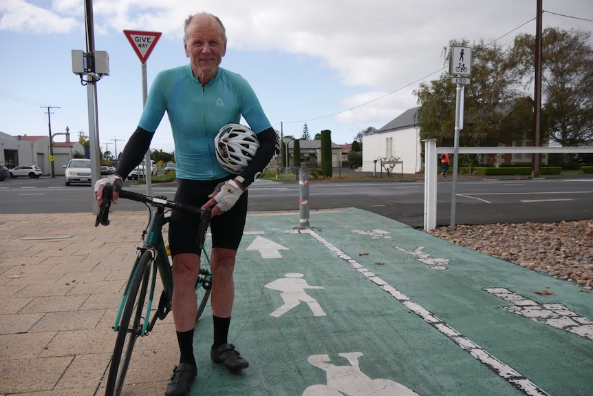 man stands with bike and helmet under arm next to path with signage