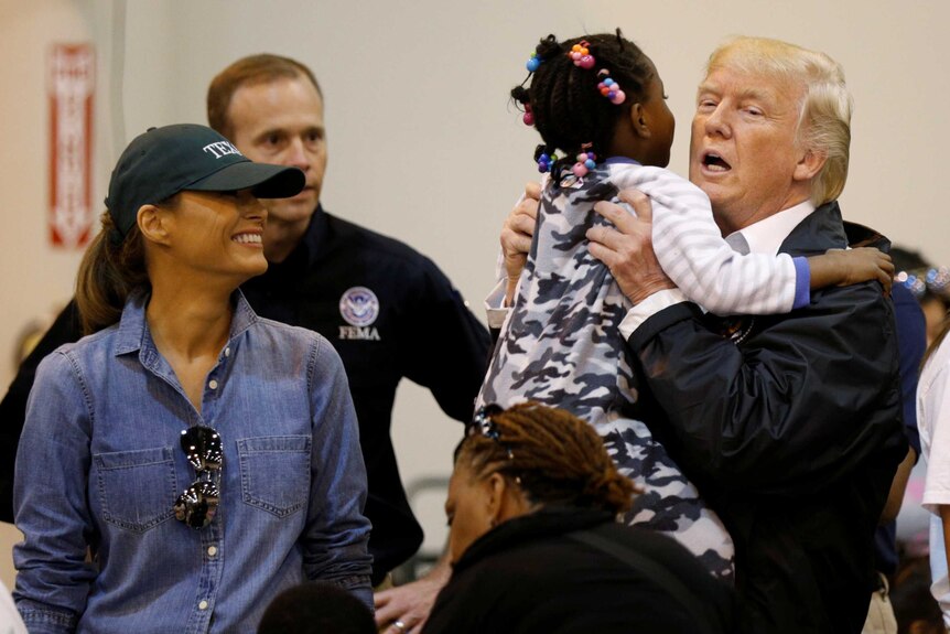 Donald Trump lifts up a little girl wearing pyjamas at a hurricane relief centre, while Melania Trump smiles