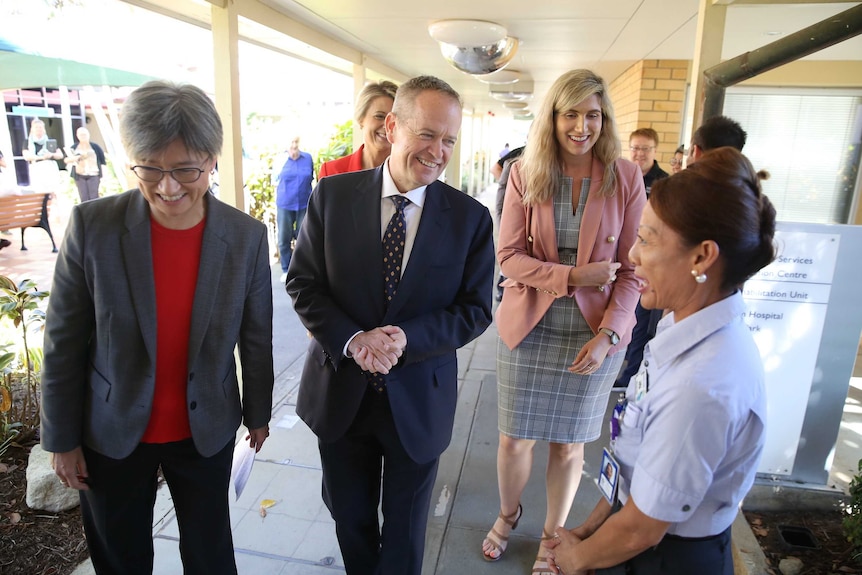 Bill Shorten holds his hands and smiles while talking to a worker. Penny Wong and Corinne Mulholland are also smiling
