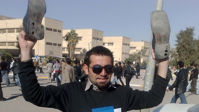 An Iraqi man holds up his shoes with an image of Muntadar al-Zaidi on his jumper