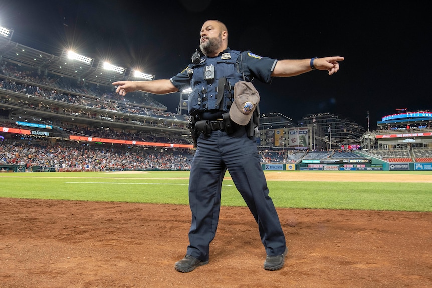 A policeman stands on an empty baseball field directing fans after gunshots were heard. outside 