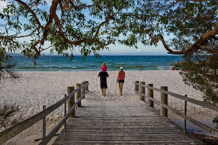 Two people walk onto the beach from a boardwalk