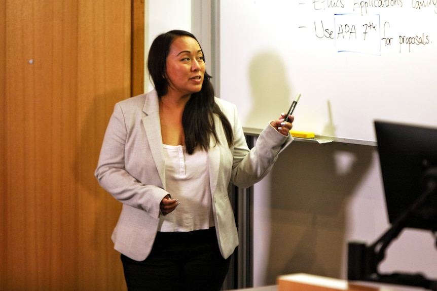 A middle-aged woman stands at a whiteboard.