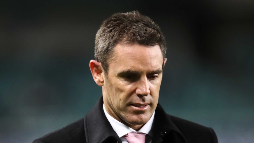 Brad Fittler walks around the sideline wearing a balck coat with his hands in his pockets looking down at the ground