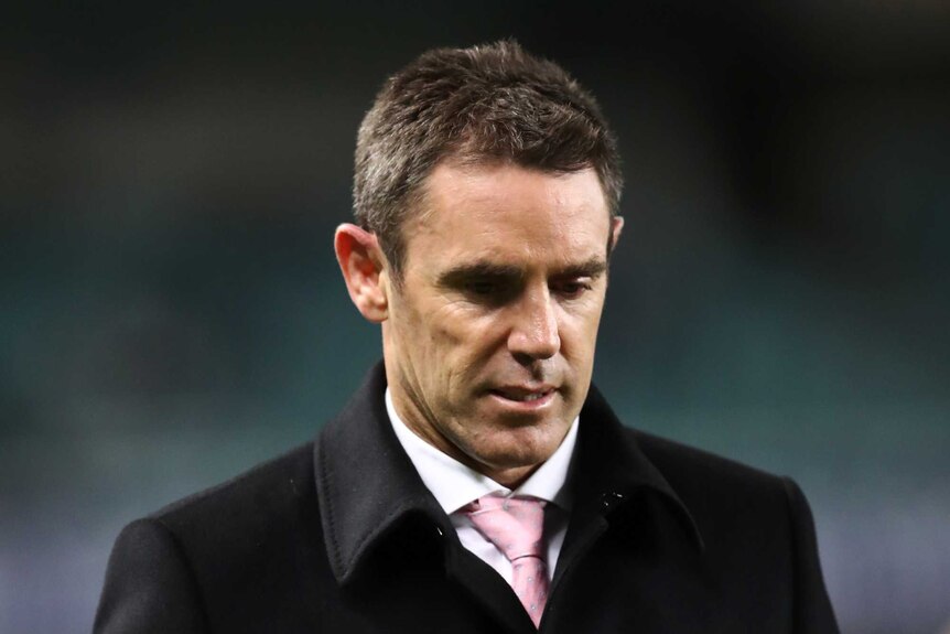Brad Fittler walks around the sideline wearing a balck coat with his hands in his pockets looking down at the ground
