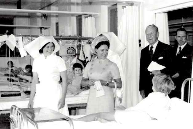 A black and white photo of a young Princess Margaret talking to child patients and nurses in a hospital ward.