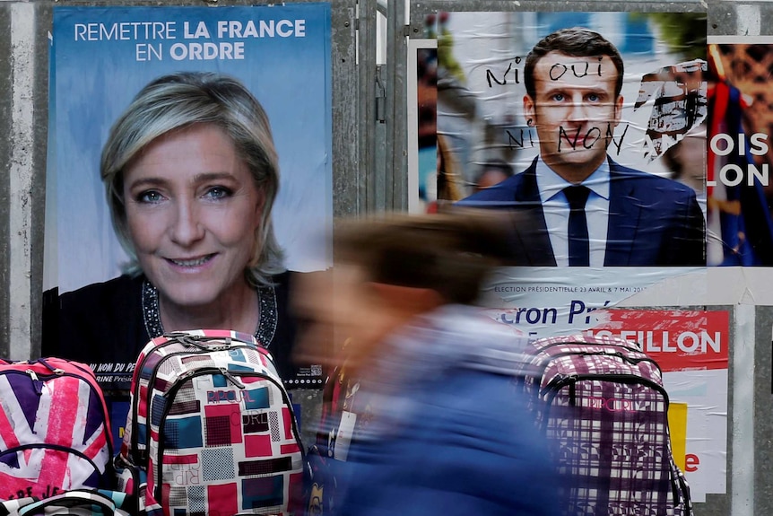 Graffitied campaign posters of Emmanuel Macron and Marine Le Pen.