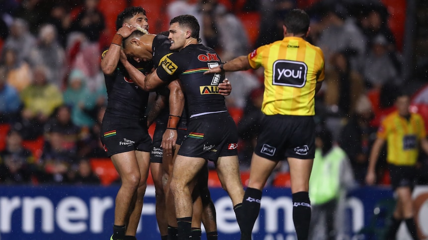 A Penrith NRL player puts his head down as his teammates hug him and the referee signals a try.