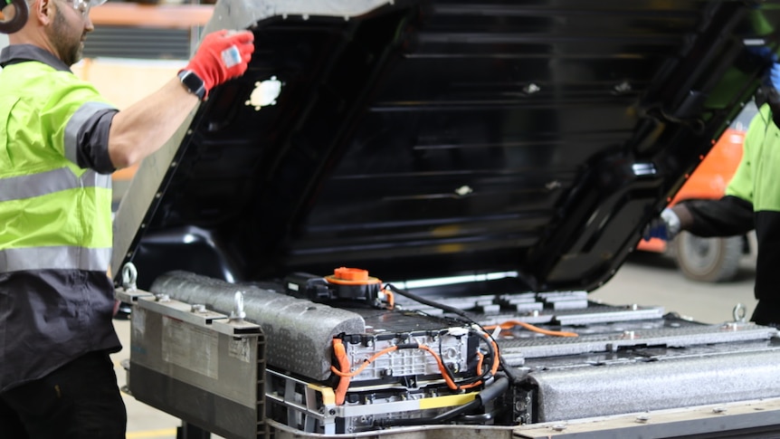 A worker lifts the top off a large grey and black battery.