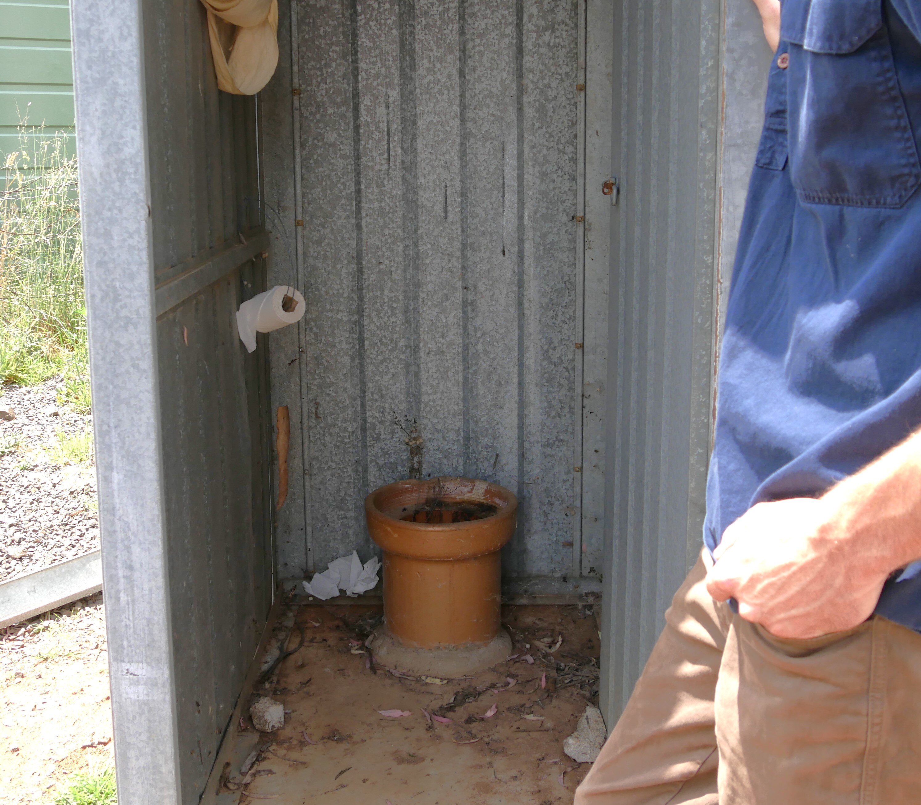 a makeshift toilet in a tin shed with a man holding the door.