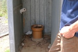 a makeshift toilet in a tin shed with a man holding the door.