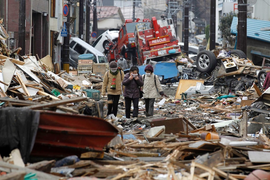 Three people walk through the ruins on a street in a Japanese city hit by the 2011 tsunami.