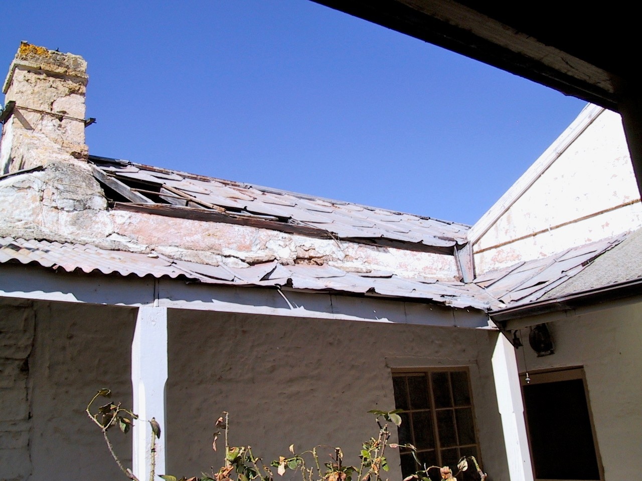 Un antiguo edificio blanco con un techo metálico que se derrumba. Hay grandes agujeros en el medio.