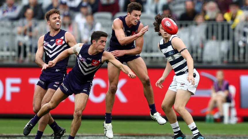 An AFL player punches the ball clear as his teammates outnumber his opponent.