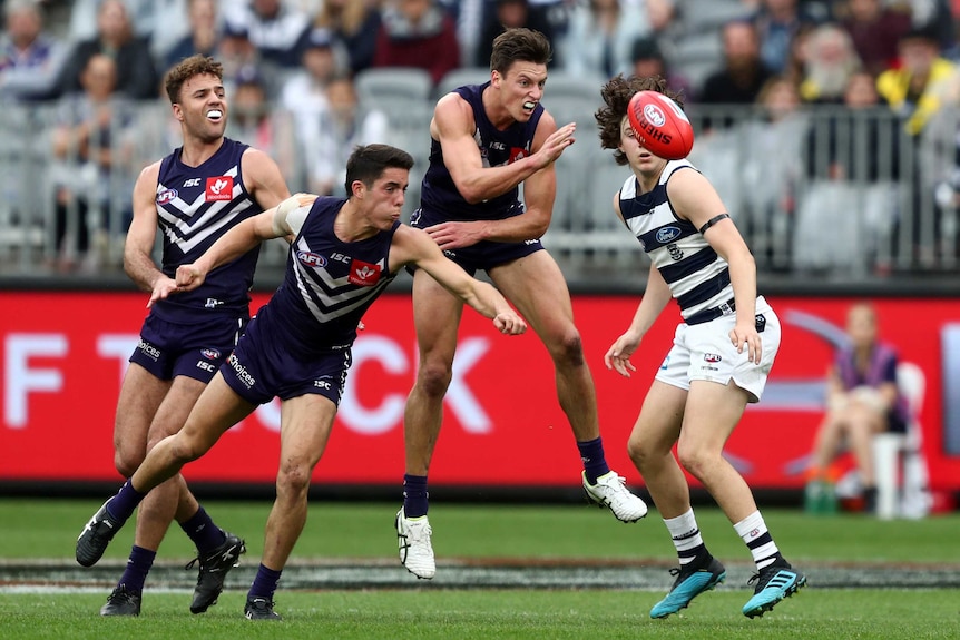 An AFL player punches the ball clear as his teammates outnumber his opponent.