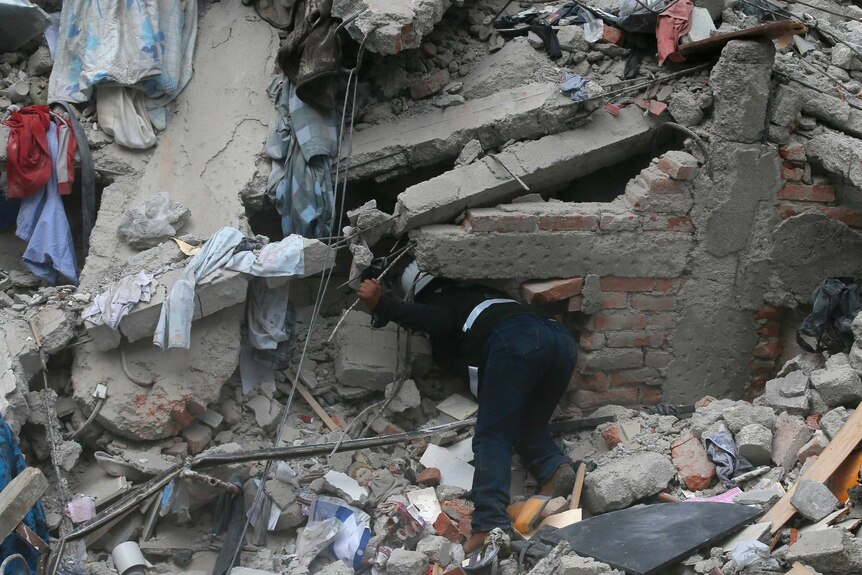 A person searches the rubble of a collapsed building.