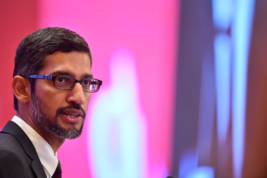 A man with glasses against a pink background.