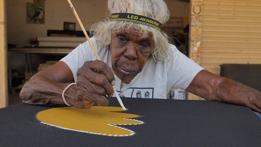 Artist wearing headband painting yellow image on black canvas.