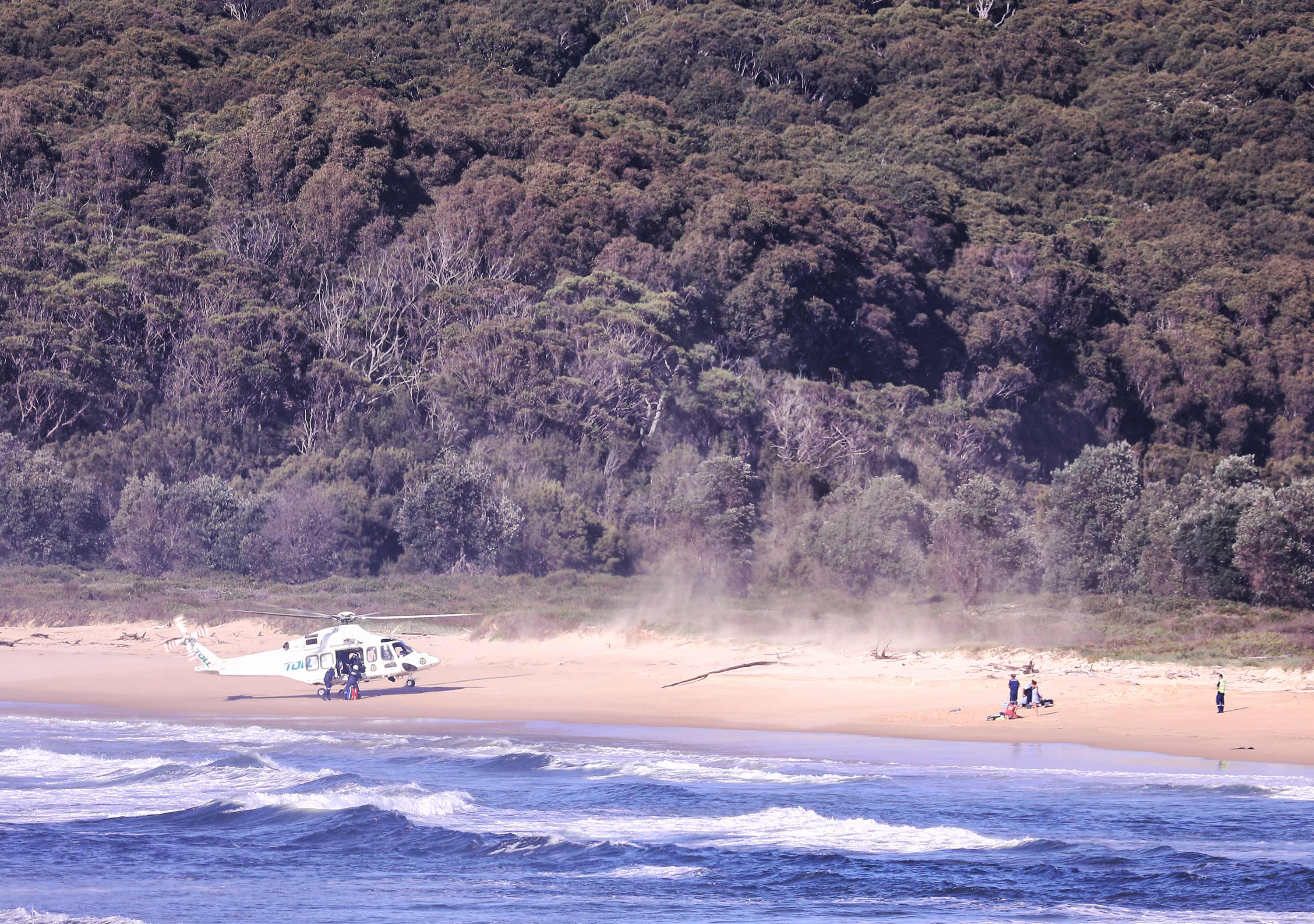 A helicopter lands on a beach near two people in need of help. 
