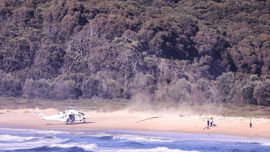 A helicopter lands on a beach near two people in need of help. 