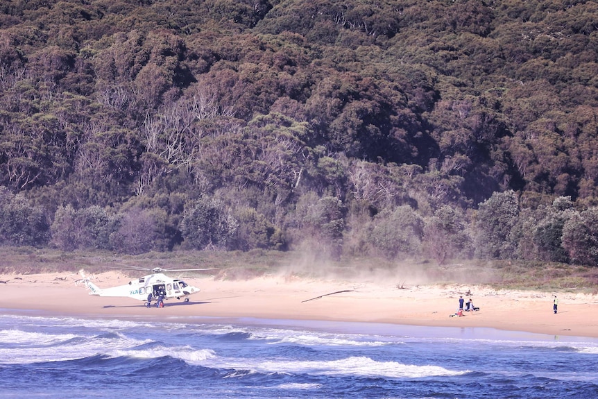 A helicopter lands on a beach near two people in need of help. 