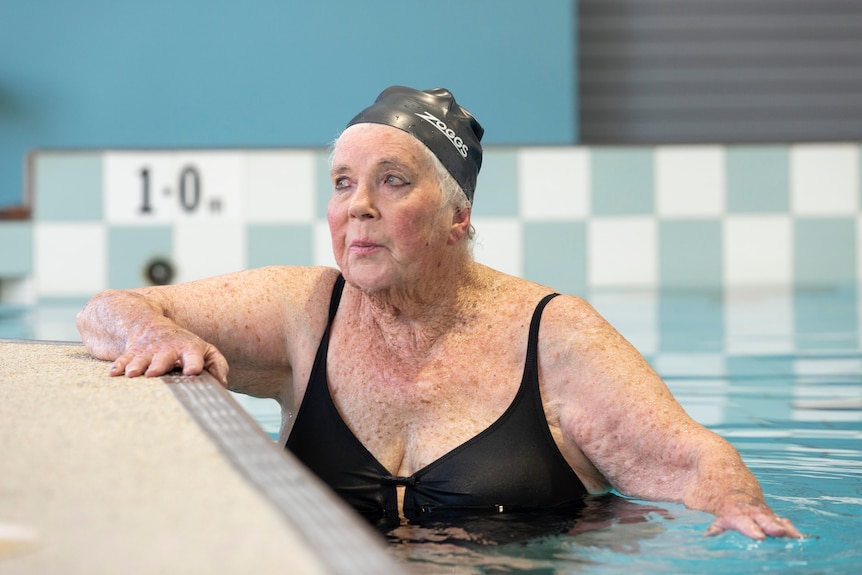 An elderely woman takes a break on the edge of the pool after swimming