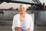 Older woman in a white top smiling in front of a bridge over water