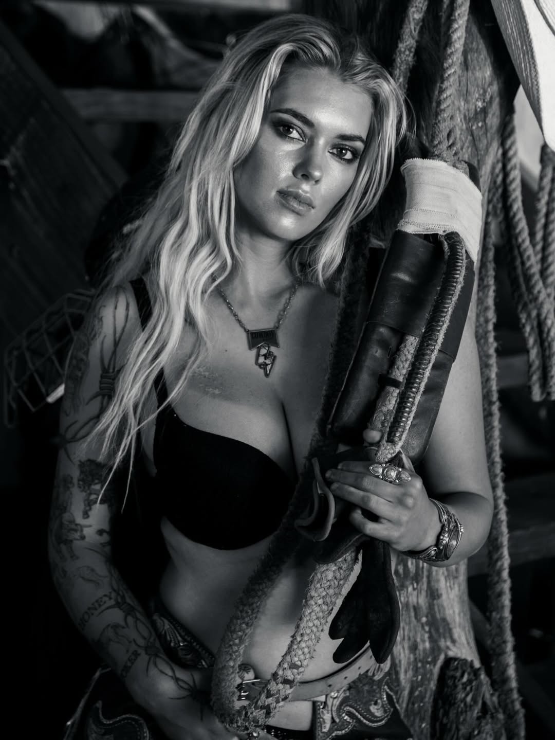 A woman with long blonde hair and a black bra holds onto a rope.