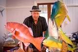 A man stands with a collection of his marine fish models, moulded from fibreglass and painted to look like the real thing.