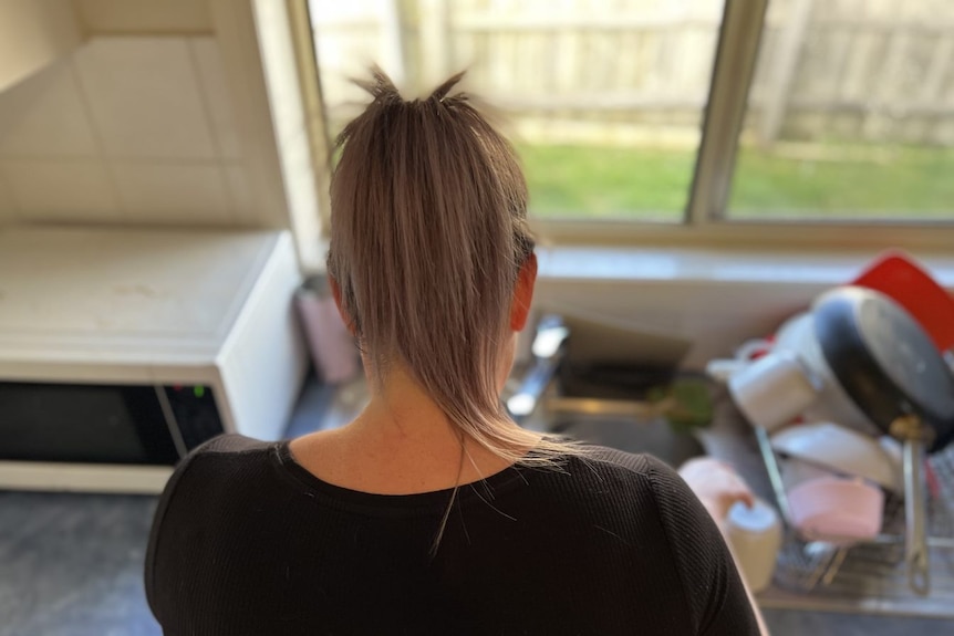 A woman is pictured from behind standing in front of her kitchen sink.