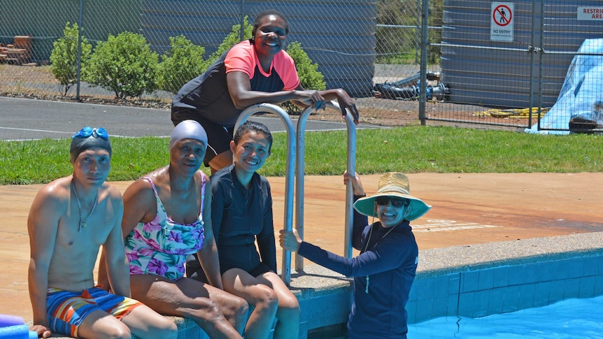 A group of multi cultural swimmers smile from the pool.