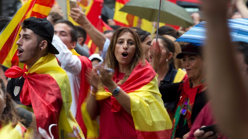 A woman draped in the Spanish flag joins other pro-Spanish unity demonstrators in clapping on Barcelona street
