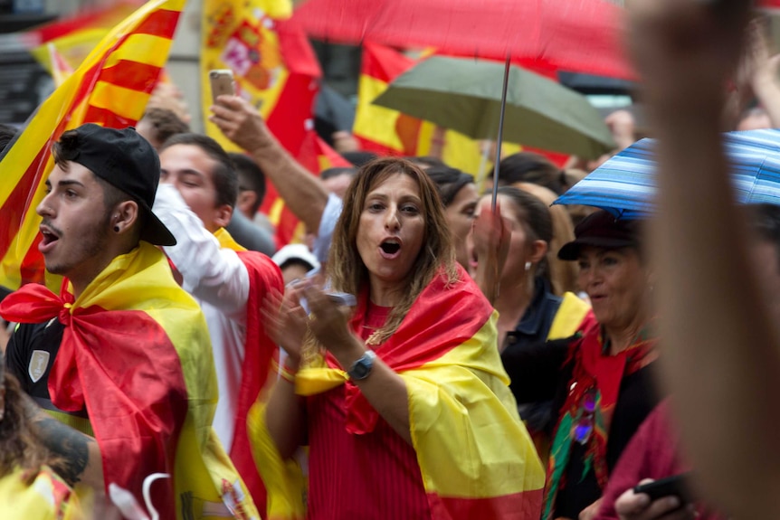 A woman draped in the Spanish flag joins other pro-Spanish unity demonstrators in clapping on Barcelona street