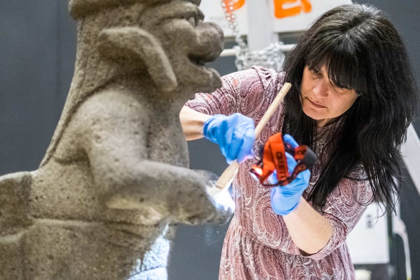 Conservator Heather McKay dusts a late-1400s stone jaguar from the Aztec exhibition