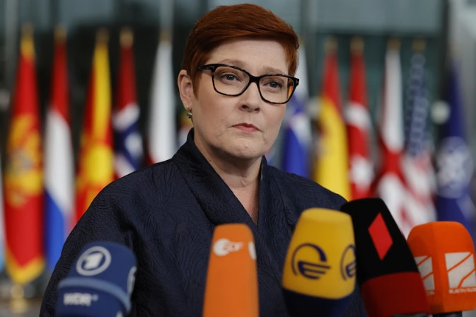 Photo of woman in glasses with flags in the background