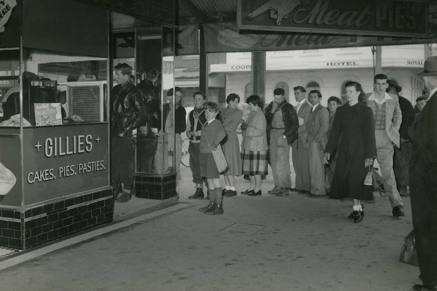 Black and white photo of people lining up at a shop