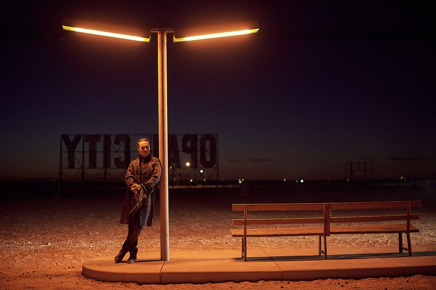 A man leans against a light post.